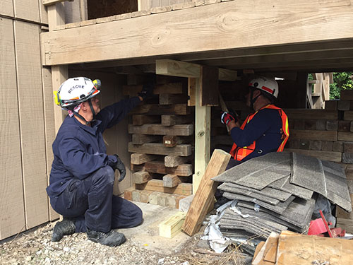 members of the Technical Rescue Team wearing hardhats in a partially enclosed space under what looks like a porch