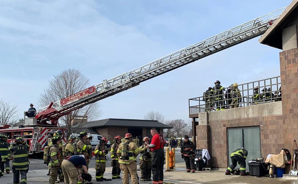 Fire Explorers in Training Fire Explorers in training gather around a fire truck with ladder extended to a roof of a nearby building