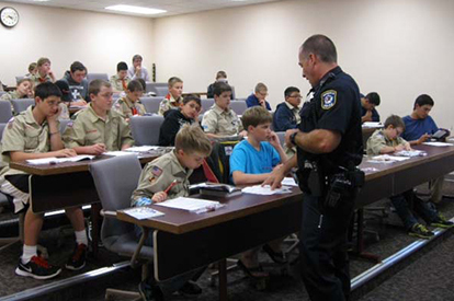 Scouts at NPD an officer teaches uniformed scouts, who are seated at long tables in a classroom setting