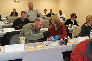 Residents seated at long tables practice dusting for prints on aluminum cans