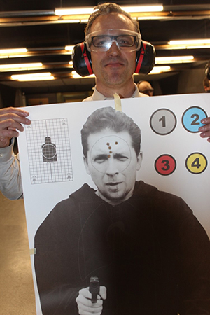 A resident wearing eye and ear protection holds up a firearms target