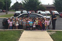 An officer poses with multiple children in front of a squad car at a day care