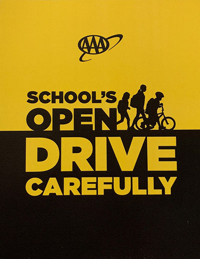 School's Open, Drive Carefully Banner an outline of children wearing backpacks walking and riding a bike with text: School's Open, Drive Carefully