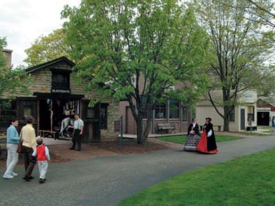 Actors in period garb walk toward residents on the streets of Naper Settlement
