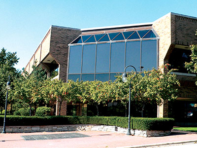 A view of Nichols Library from the parking lot reveals a brick structure with a towering wall of glass surrounded by trees.
