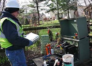 A worker clad in a hardhat and safety vest holds a clipboard in front of an electrical box getting ready to start the 2017 cable injection project